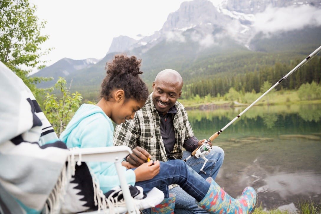 A man and girl fishing on the shore of a lake.