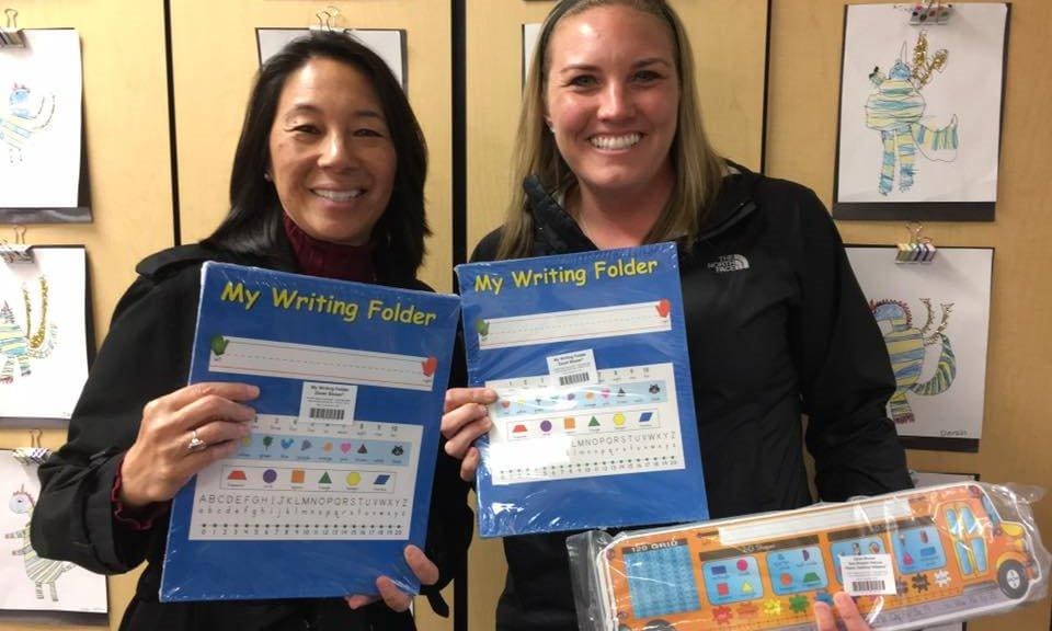 Two women holding up their writing folders